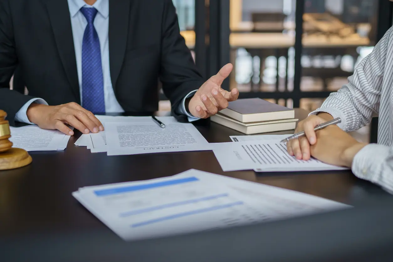 BusinessImage Two professionals in a meeting. One in a suit gestures while the other in a striped shirt takes notes. Papers and a gavel are on the table, conveying a legal or business discussion.